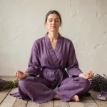 Femme méditant en robe violette entourée de cristaux d'améthyste symbolisant l'aura violette et le chakra coronal